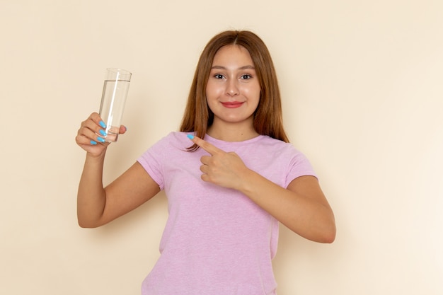 ピンクのtシャツと笑顔で水のガラスを保持しているブルージーンズの正面の若い魅力的な女性
