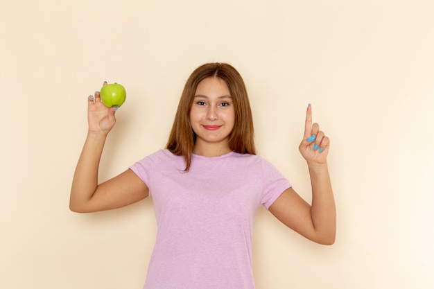 Front view young attractive female in pink t-shirt and blue jeans holding green apple with smile