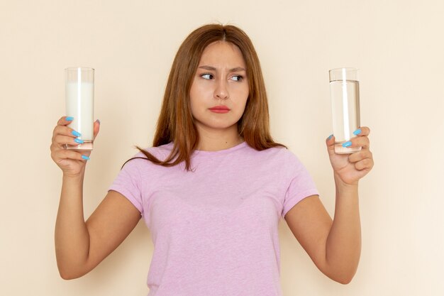 Вид спереди молодая привлекательная женщина в розовой футболке и синих джинсах, держащая молоко и воду
