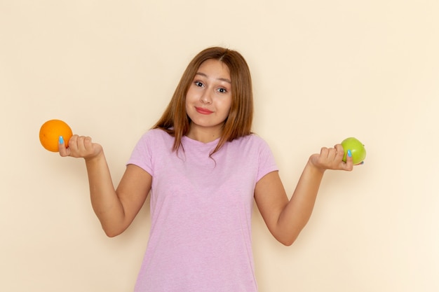 ピンクのtシャツとブルージーンズにオレンジとリンゴを保持している正面の若い魅力的な女性