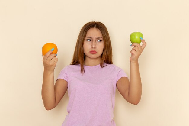 Front view young attractive female in pink t-shirt and blue jeans holding orange and apple