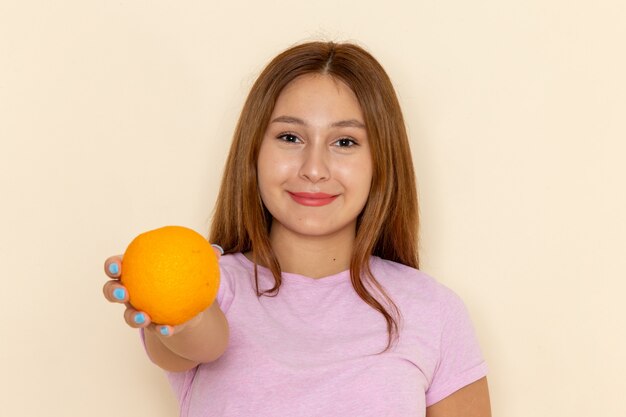 Front view young attractive female in pink t-shirt and blue jeans holding orange and giving it away