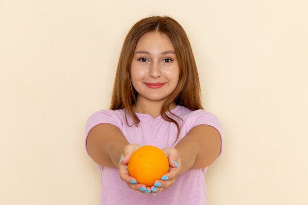 Front view young attractive female in pink t-shirt and blue jeans holding orange and giving it