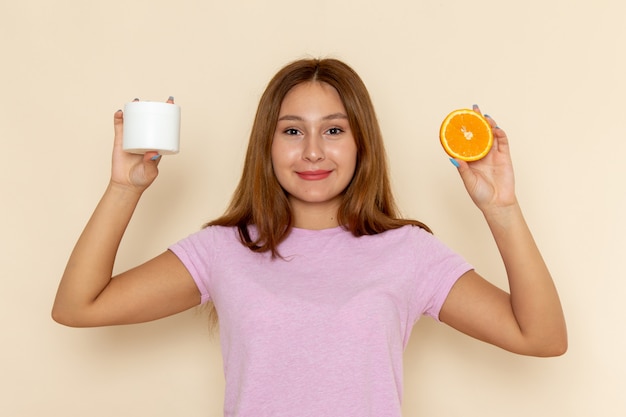 Free photo front view young attractive female in pink t-shirt and blue jeans holding orange