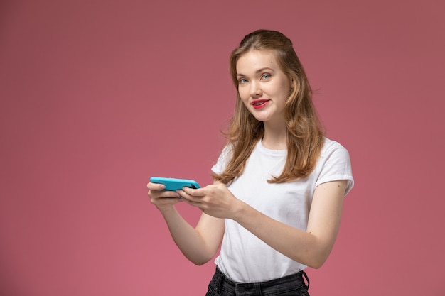 Front view young attractive female playing game via her phone on the pink wall model color female young