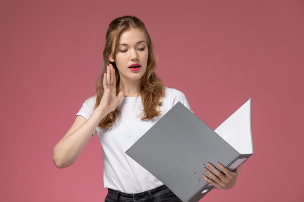 Front view young attractive female reading and holding grey file on the pink wall model color female young