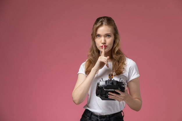 Front view young attractive female showing silence sign holding remote controller on pink wall model color female young girl