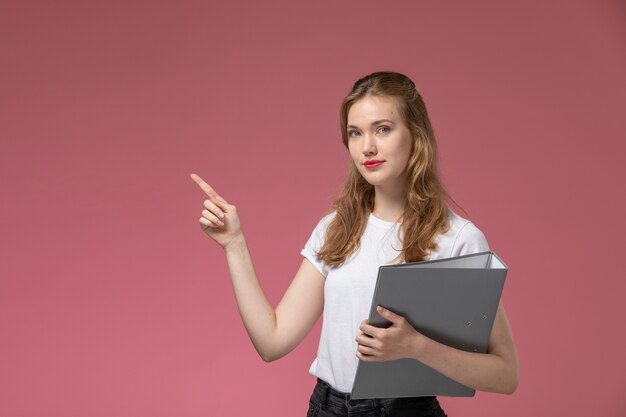 Front view young attractive female smiling holding grey document on the pink wall model color female young girl