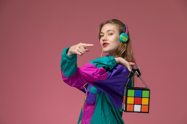 Foto gratuita vista frontale giovane femmina attraente che indossa cappotto colorato ascoltando musica sulla parete rosa scuro modello colore femmina giovane ragazza