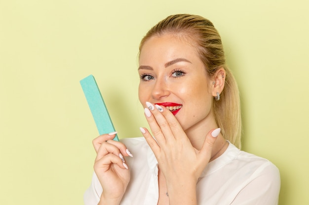 Front view young attractive female in white shirt fixing her nails on green surface