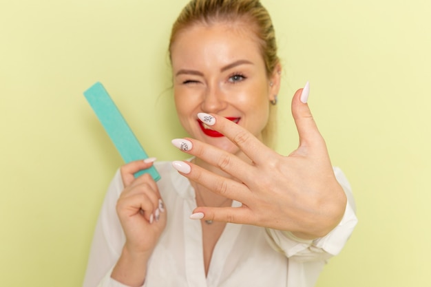 Front view young attractive female in white shirt fixing her nails on green surface