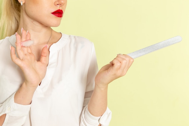 Foto gratuita giovane femmina attraente di vista frontale in camicia bianca che ripara le sue unghie sulla superficie verde chiaro