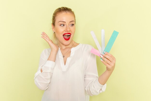 Front view young attractive female in white shirt holding different manicure accessories on light-green surface