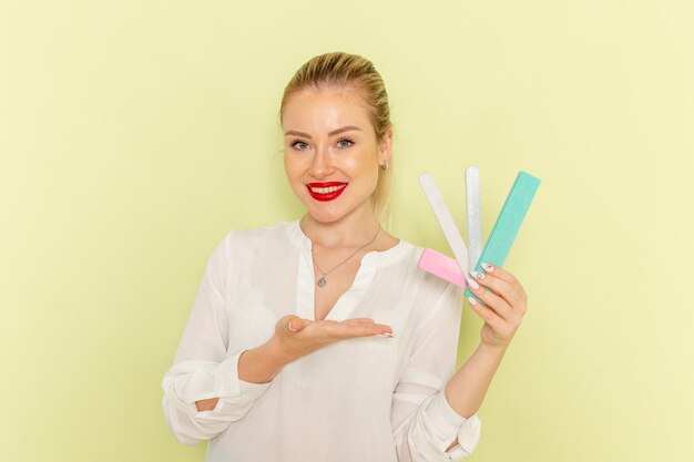 Front view young attractive female in white shirt holding different manicure accessories with smile on green surface