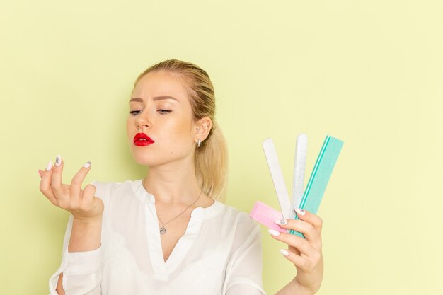 Front view young attractive female in white shirt holding manicure accessories on the green surface