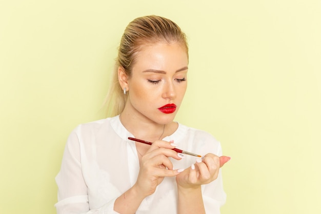 Front view young attractive female in white shirt working with her nails on green surface