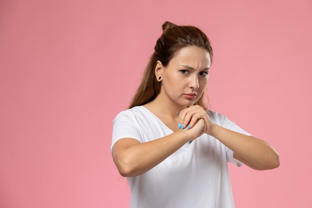 ピンクの背景の白いtシャツの怒りの表現で正面の若い魅力的な女性