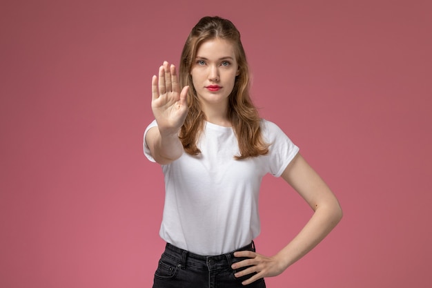 Front view young attractive female in white t-shirt and black trousers posing showign stop sign on the pink wall model female pose color photo