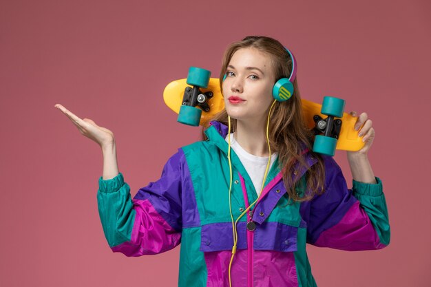 Front view young attractive female in white t-shirt colored coat holding skateboard on the pink wall model female young