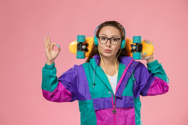 Free photo front view young attractive female in white t-shirt and colored coat listening to music on the pink background