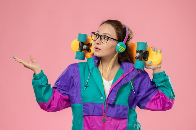 ピンクの背景で音楽を聴く白いtシャツ色のコートの正面若い魅力的な女性