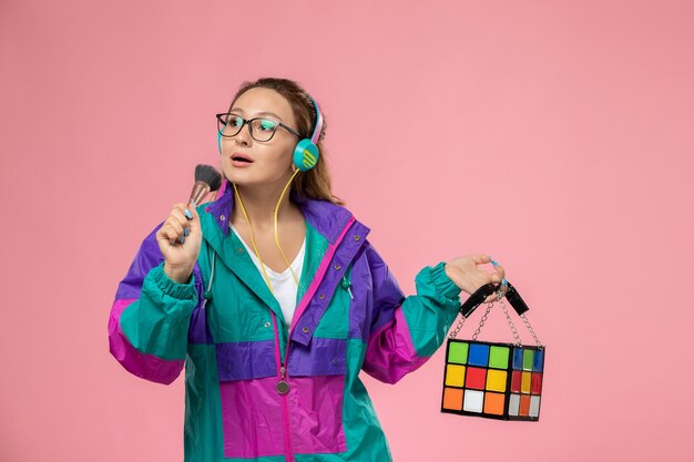 ピンクの背景で音楽を聴く白いtシャツ色のコートの正面若い魅力的な女性