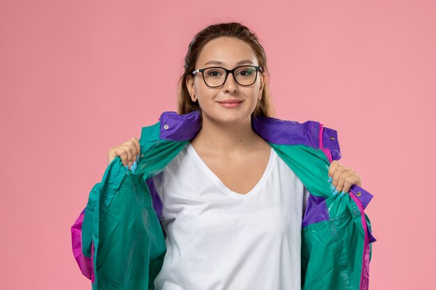 ピンクの背景に少し笑顔でポーズをとって白いtシャツの色のコートで正面の若い魅力的な女性