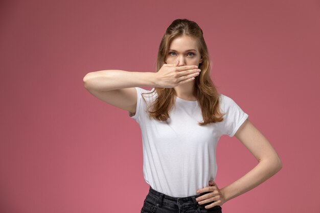 Front view young attractive female in white t-shirt covering her mouth on the dark-pink wall model color female young girl
