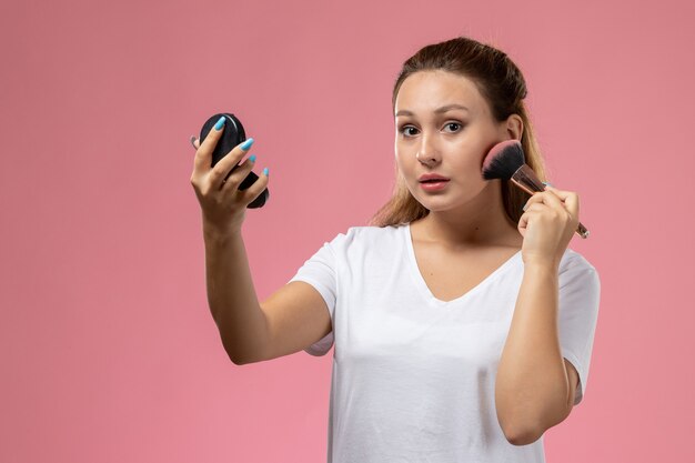 ピンクの背景にカメラに探している化粧をしている白いtシャツの正面若い魅力的な女性