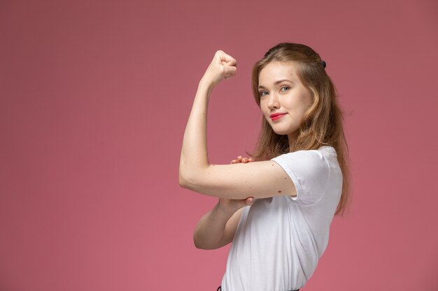 Front view young attractive female in white t-shirt flexing on the dark-pink wall model color female young girl