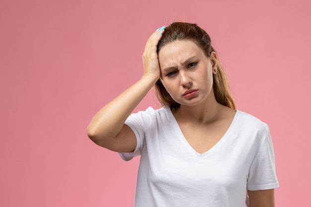 Front view young attractive female in white t-shirt having a severe headache on the pink background