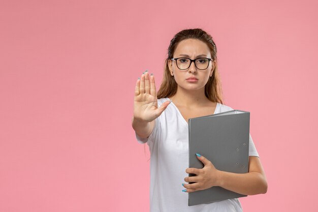 ピンクの背景に灰色の色のファイルを保持している白いtシャツの正面の若い魅力的な女性