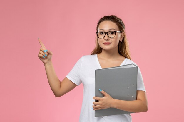 Front view young attractive female in white t-shirt holding grey document on the pink background