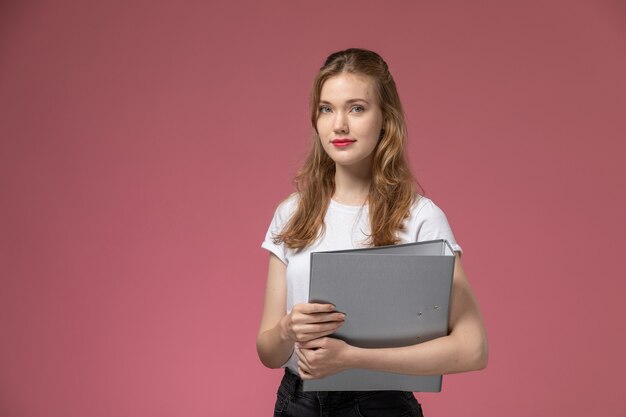 Front view young attractive female in white t-shirt holding grey file on pink wall model color female young