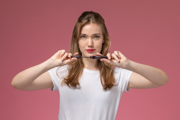 Front view young attractive female in white t-shirt holding mascara on the dark-pink wall model color female young girl