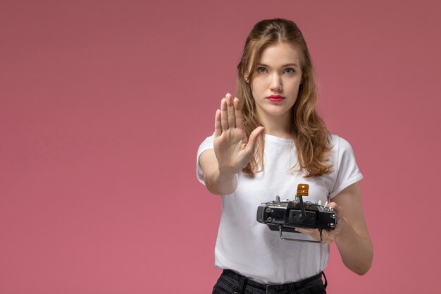 Front view young attractive female in white t-shirt holding remote controller showing stop sign on the pink wall model color female young