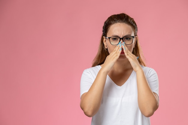 Free photo front view young attractive female in white t-shirt just posing and covering her nose on the pink background