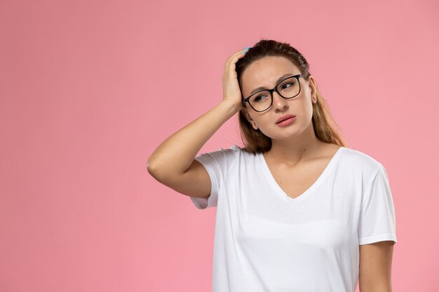 ちょうどポーズとピンクの背景に頭痛を持っている白いtシャツで正面の若い魅力的な女性