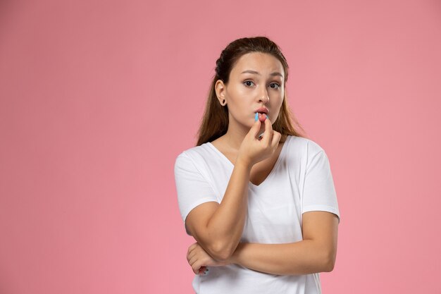 Front view young attractive female in white t-shirt just posing touching her lips on the pink background