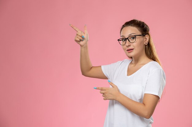 Front view young attractive female in white t-shirt just posing with raised hands on the pink background