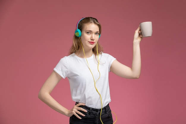 Free photo front view young attractive female in white t-shirt listening to music holding cup with smile on the pink wall model color female young girl