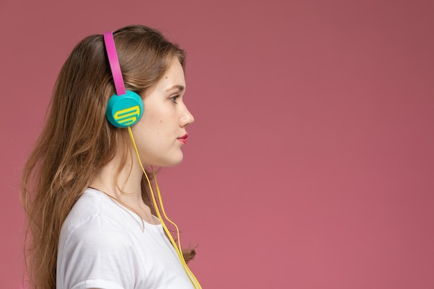 Front view young attractive female in white t-shirt listening to music with turned hair on the dark-pink wall model color female young girl