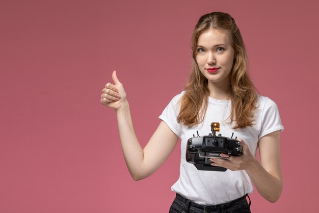 Front view young attractive female in white t-shirt posing holding remote controller on pink wall model color female young