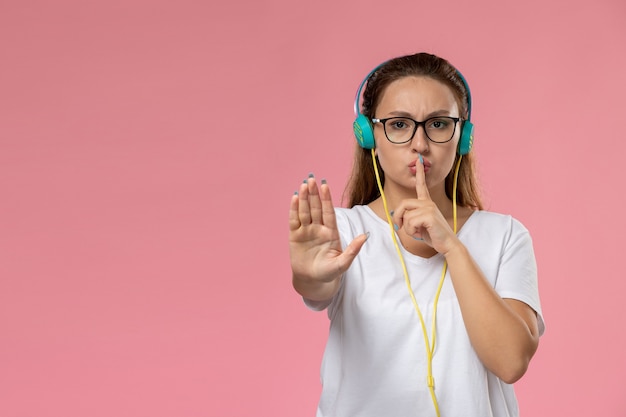 Front view young attractive female in white t-shirt posing listening to music on the pink background