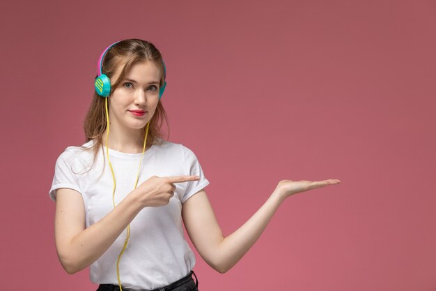 Front view young attractive female in white t-shirt posing and listening to music with smile on pink wall model female pose color photo