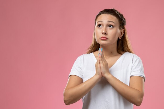 Front view young attractive female in white t-shirt posing and praying on the pink background