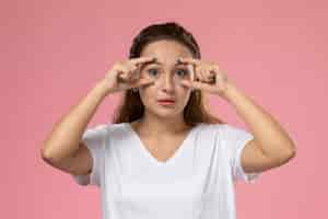 Free photo front view young attractive female in white t-shirt posing showing her eyes on the pink background