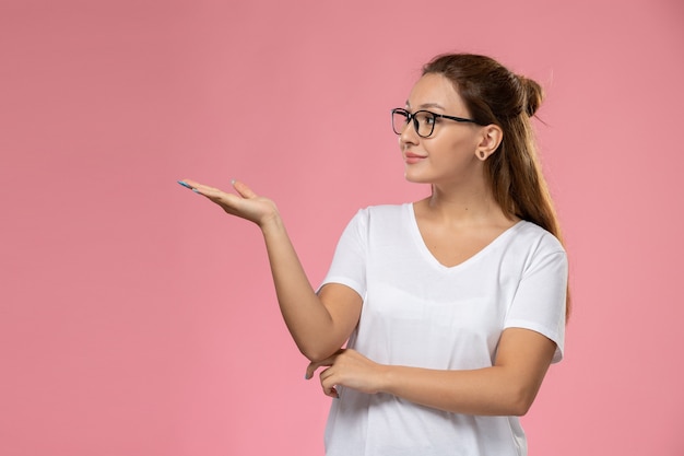 ピンクの背景に白いtシャツのポーズとsmiで正面の若い魅力的な女性