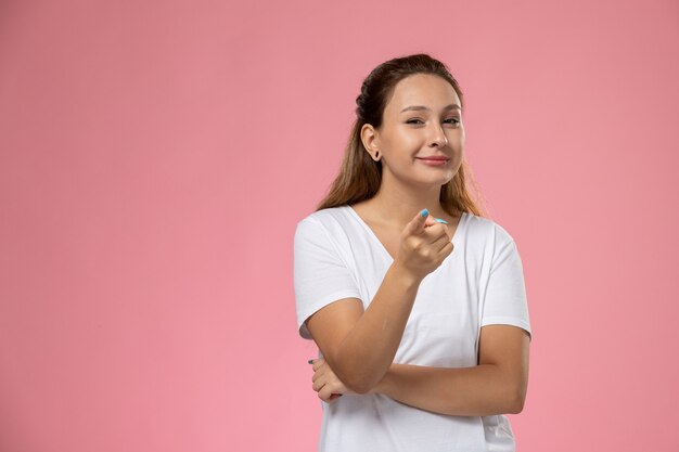 ピンクの背景に白いtシャツのポーズとsmiで正面の若い魅力的な女性