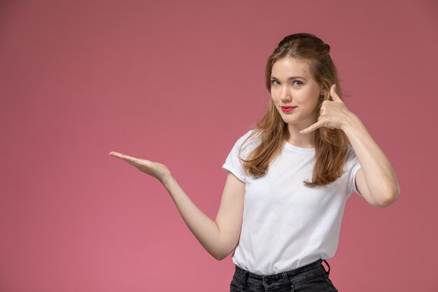 Front view young attractive female in white t-shirt posing with phone call gesture on the pink wall model female pose color photo